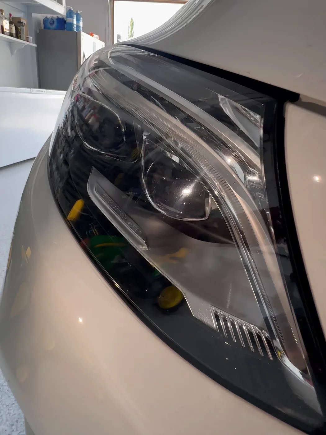 Mercedes headlight lens after polishing, garage reflected in the lens
